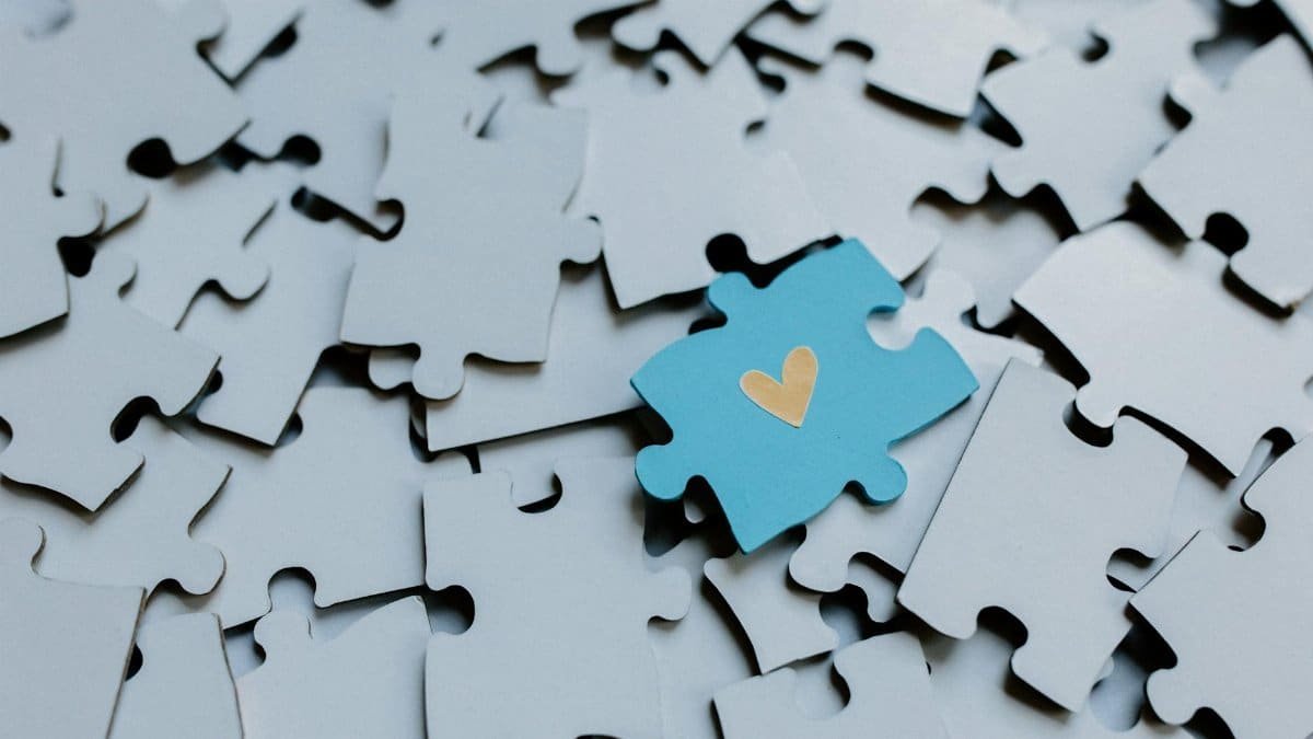 A single blue puzzle piece with a heart amid scattered pieces, symbolizing connection.