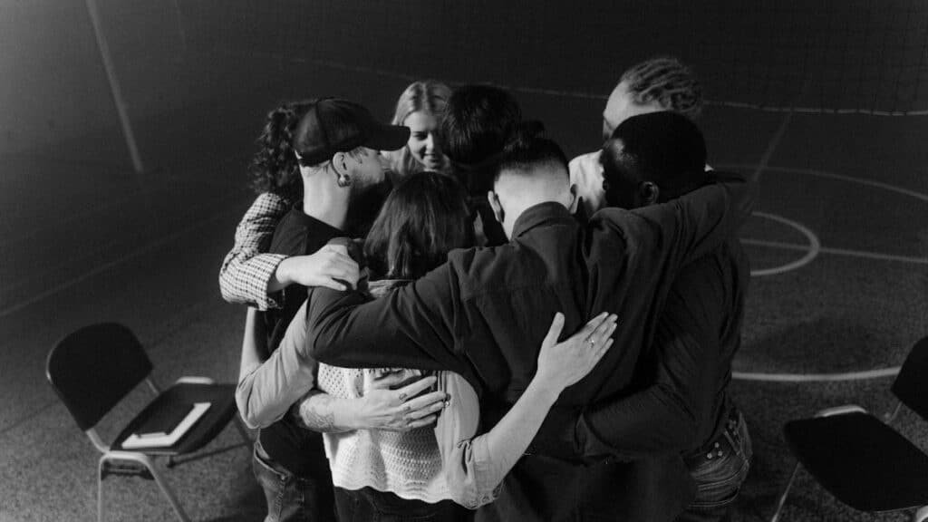 A diverse group in a supportive embrace during a meeting, symbolizing unity and connection.