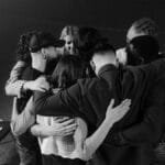 A diverse group in a supportive embrace during a meeting, symbolizing unity and connection.
