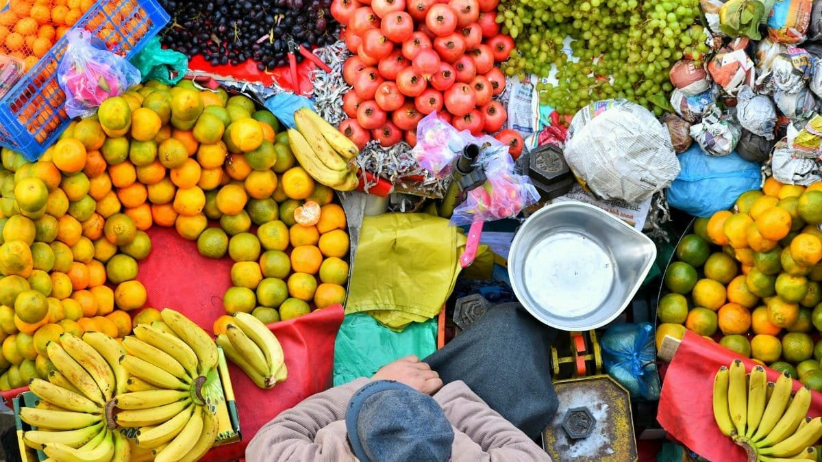 Colorful fruit market stall viewed from above showcasing a diverse array of fruits including bananas, grapes, and oranges.