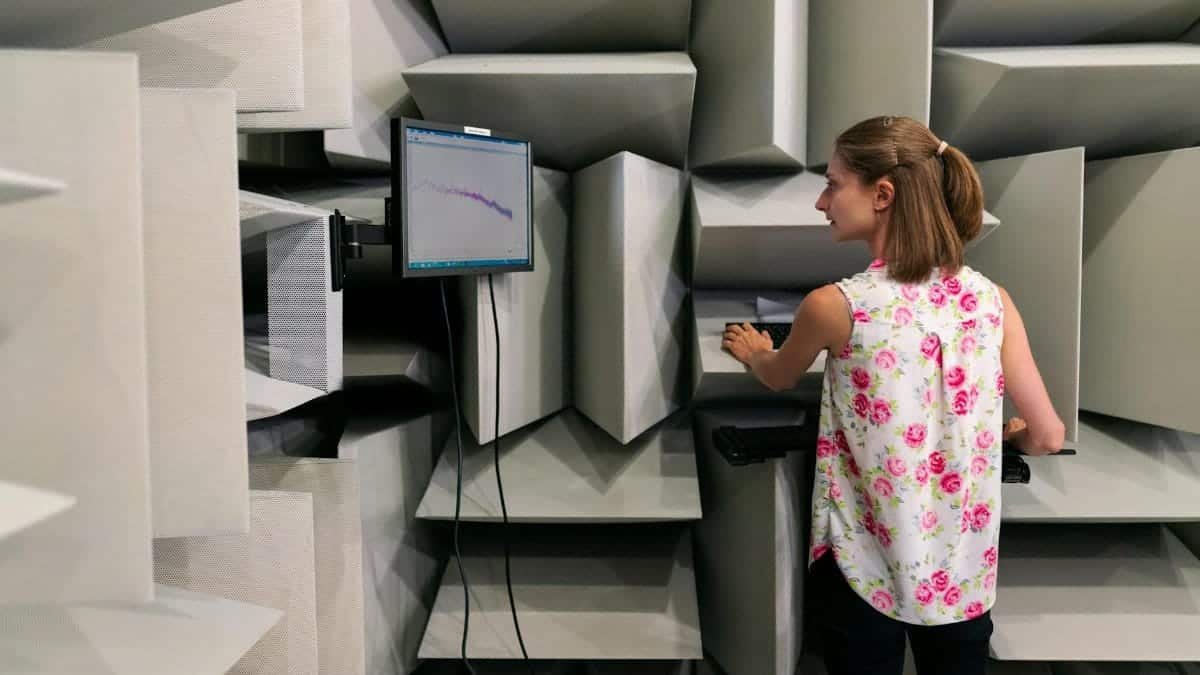 Female engineer testing sound waves in an anechoic chamber with a monitor.