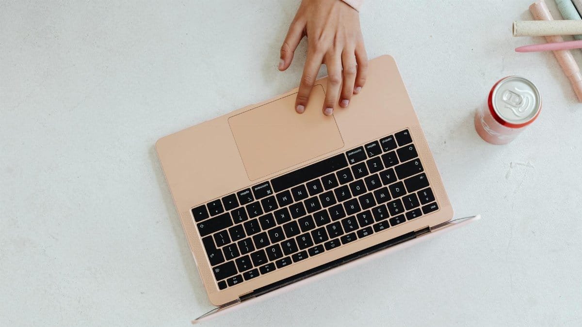 A person using a laptop on a white surface, next to a soda can and colored pencils.