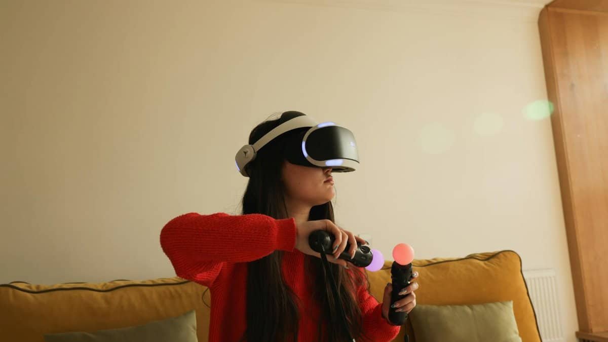 Woman playing VR game with headset and controllers in a cozy indoor setting.