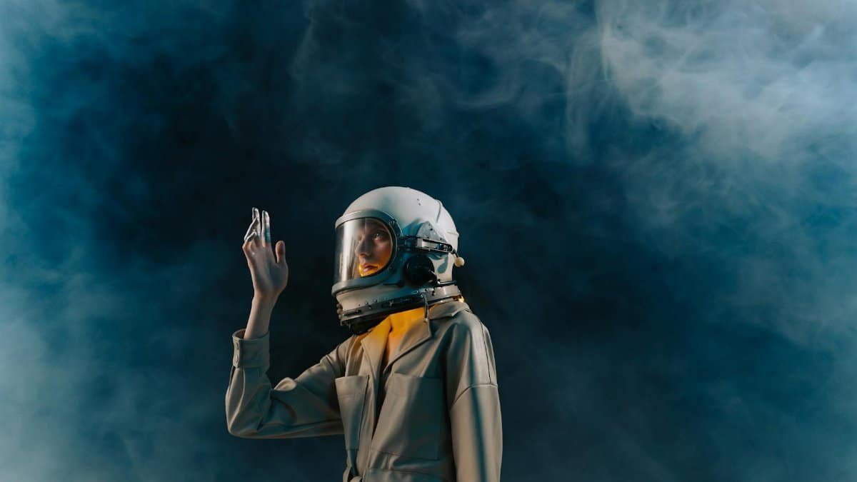 A modern astronaut in a spacesuit raises their hand amidst ethereal smoke, blue tones.