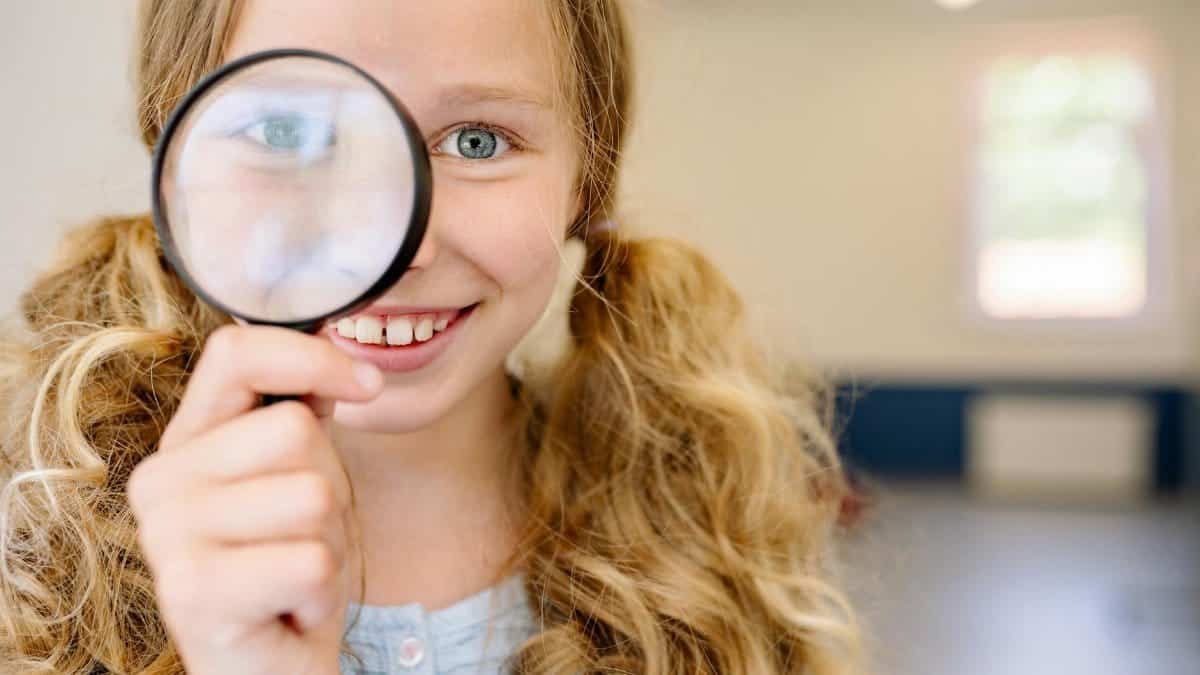 Smiling young girl looking through a magnifying glass indoors, exploring her curiosity.