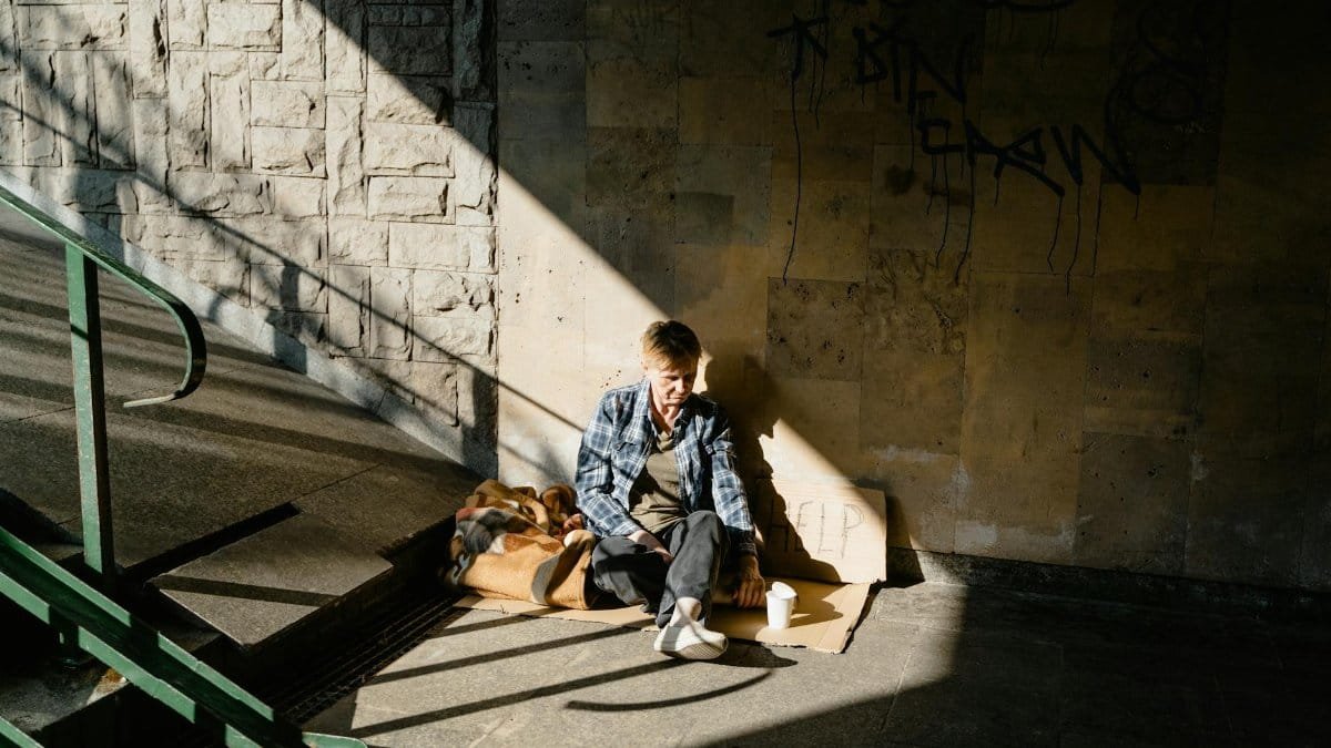 A homeless person sitting in a sunlit urban area, highlighting social issues.