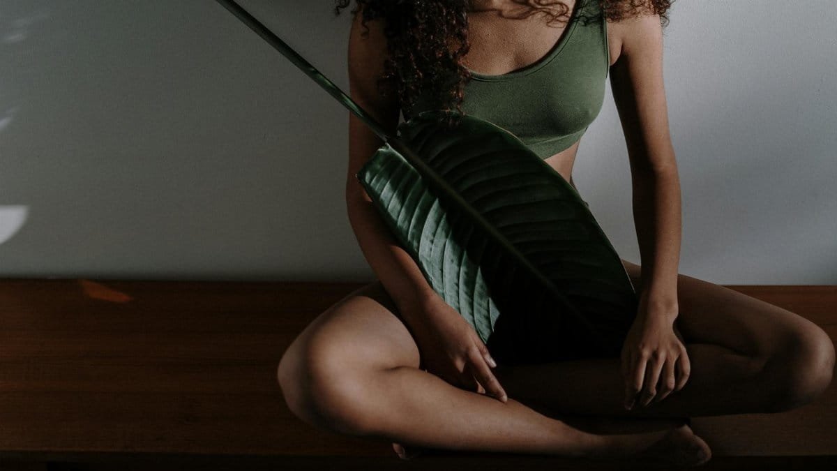 A serene photo of a woman meditating indoors, holding a large tropical leaf.