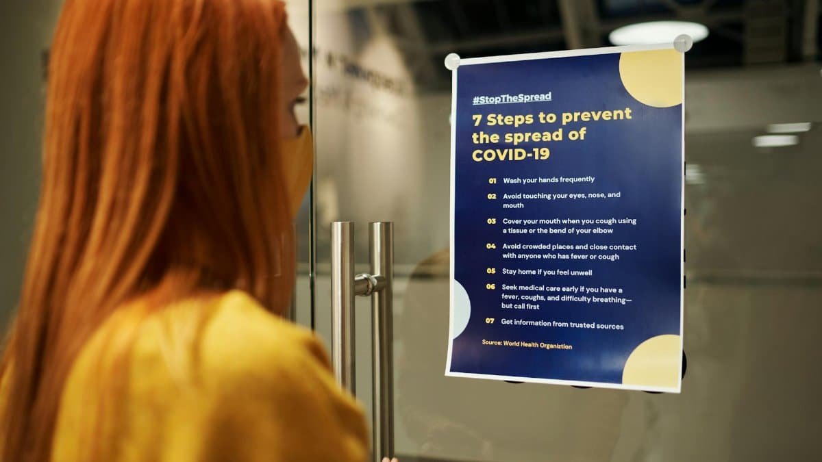 A woman reads a COVID-19 prevention poster emphasizing safety guidelines indoors.