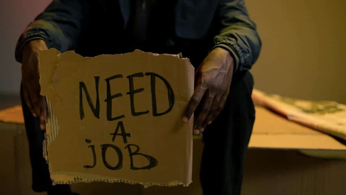 A man holding a cardboard sign reading 'Need a Job', symbolizing unemployment and hardship.