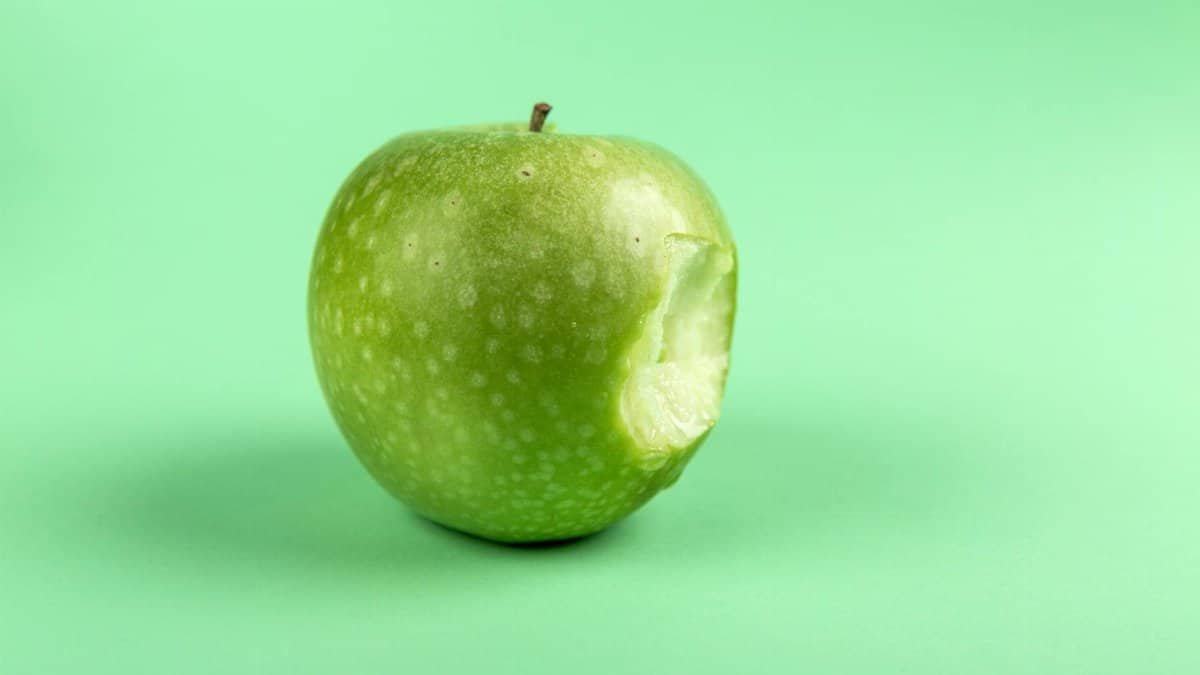 A fresh, bitten green apple on a simple green surface. Perfect for health and food-themed design.