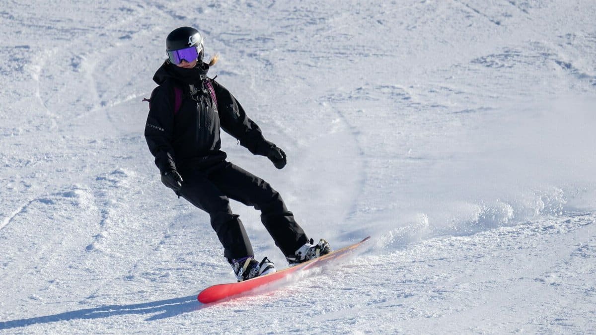 A snowboarder in black gear skillfully navigates a snowy slope during winter daytime.