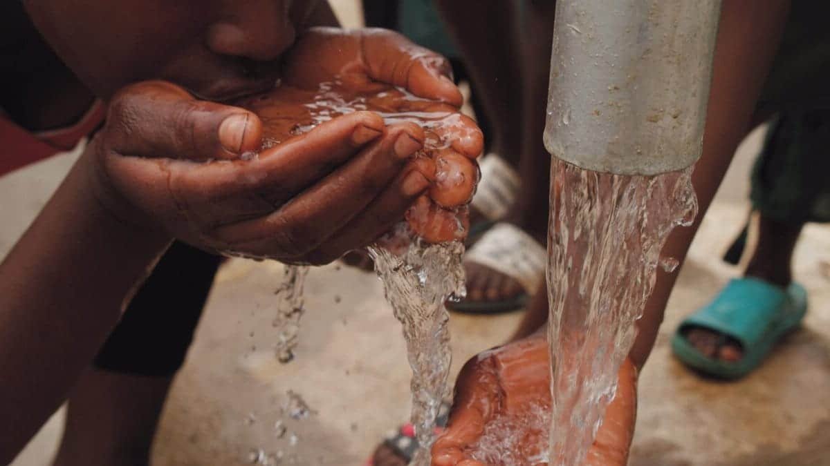 Close-up of hands and face drinking fresh water from an outdoor tap, emphasizing refreshment and necessity.