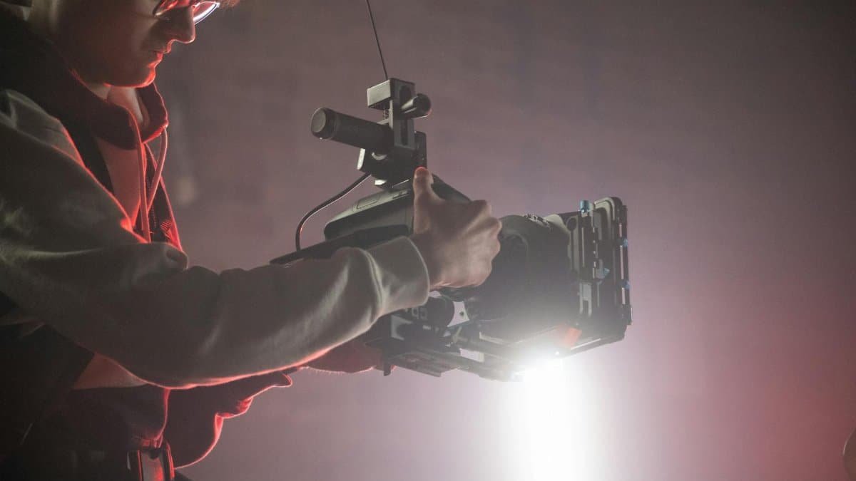 Cameraman using an Easyrig to film in a dimly lit studio with spotlight effects.