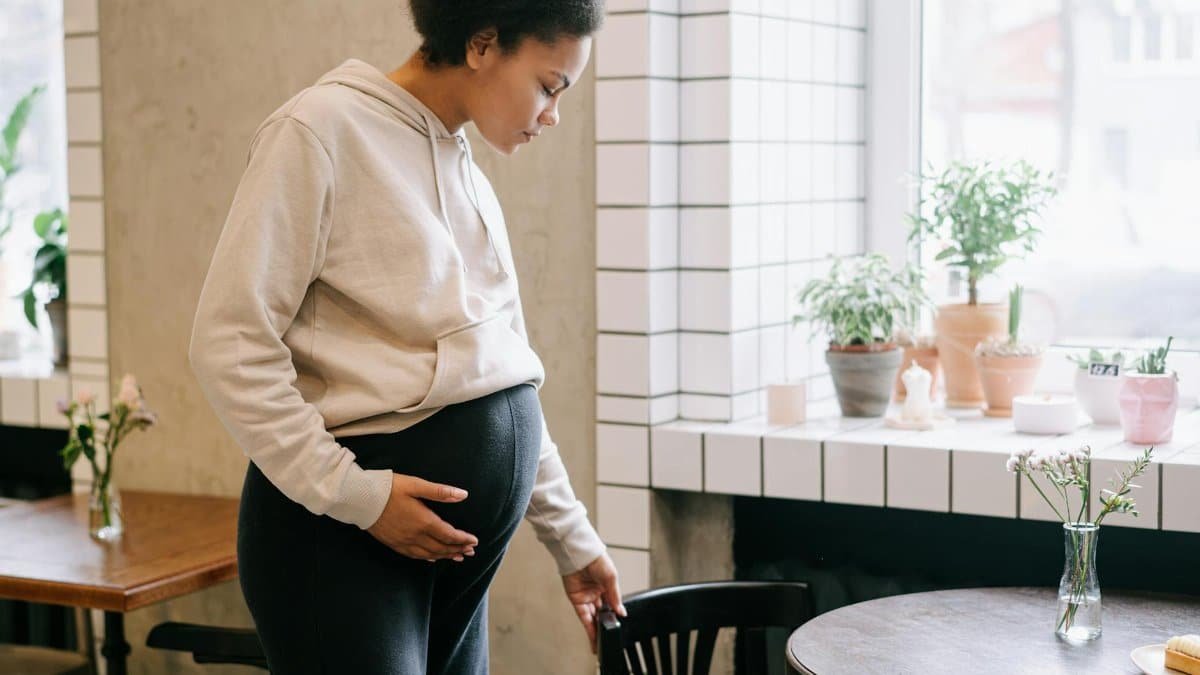 African American pregnant woman in a cozy cafe interior with plants and wooden furniture.