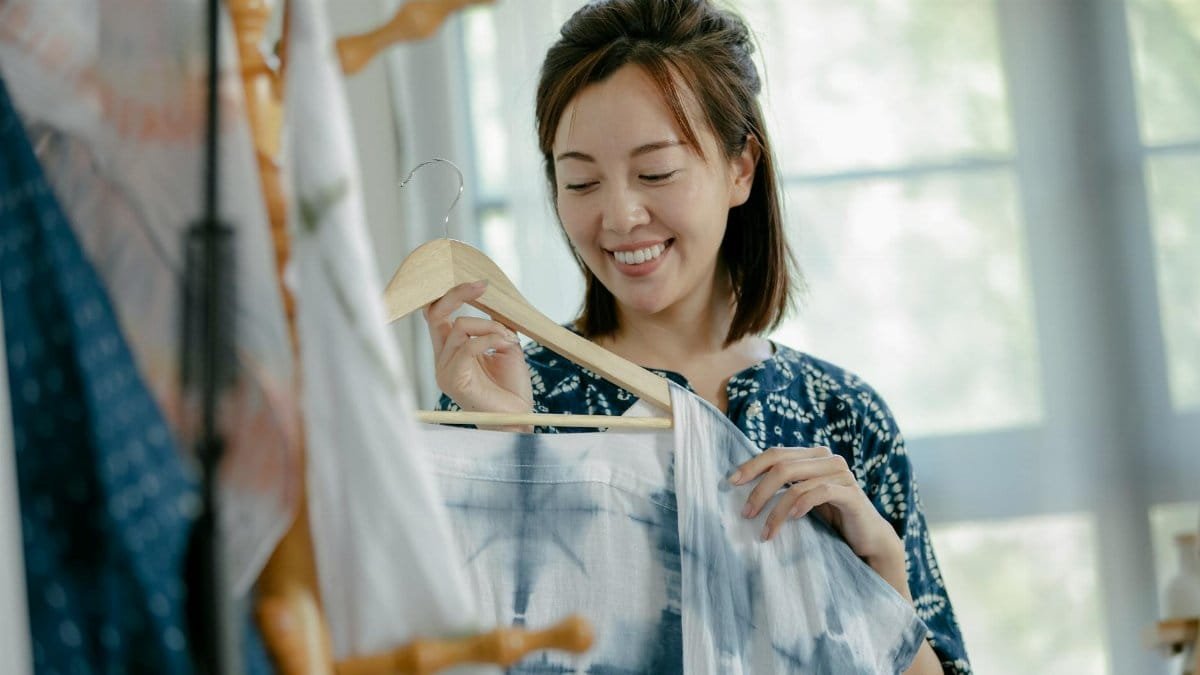A cheerful Asian woman showcasing beautiful tie-dye fabric in a bright studio.