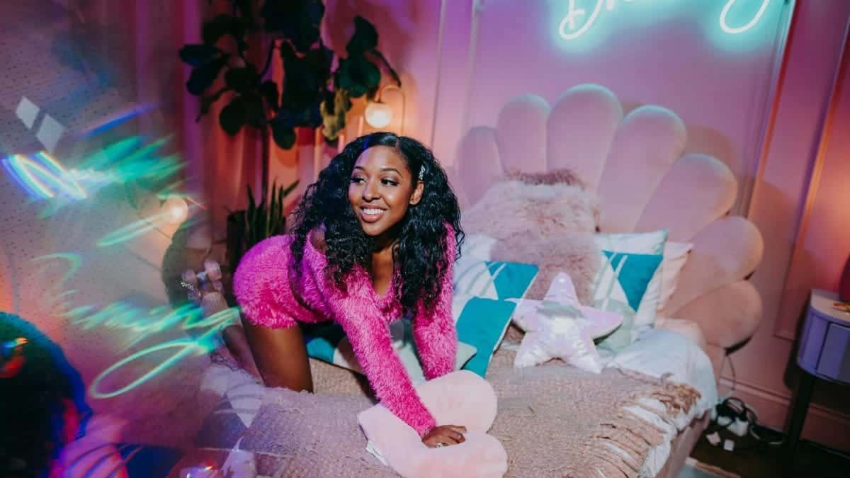 Young woman in a colorful bedroom with neon lights and cozy decor.