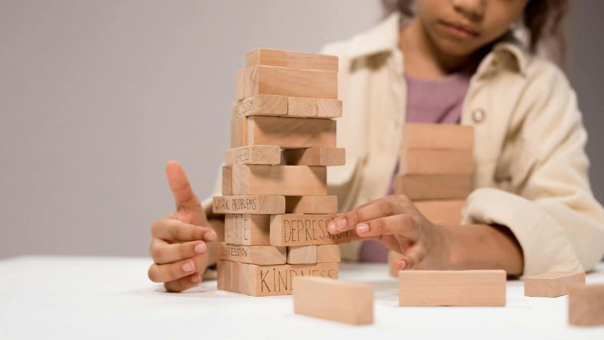 A child thoughtfully stacks wooden blocks with words like 'depression' and 'kindness.'