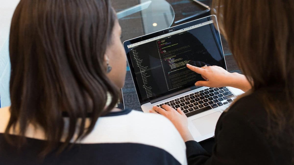 Two women working together on software programming indoors, focusing on code.