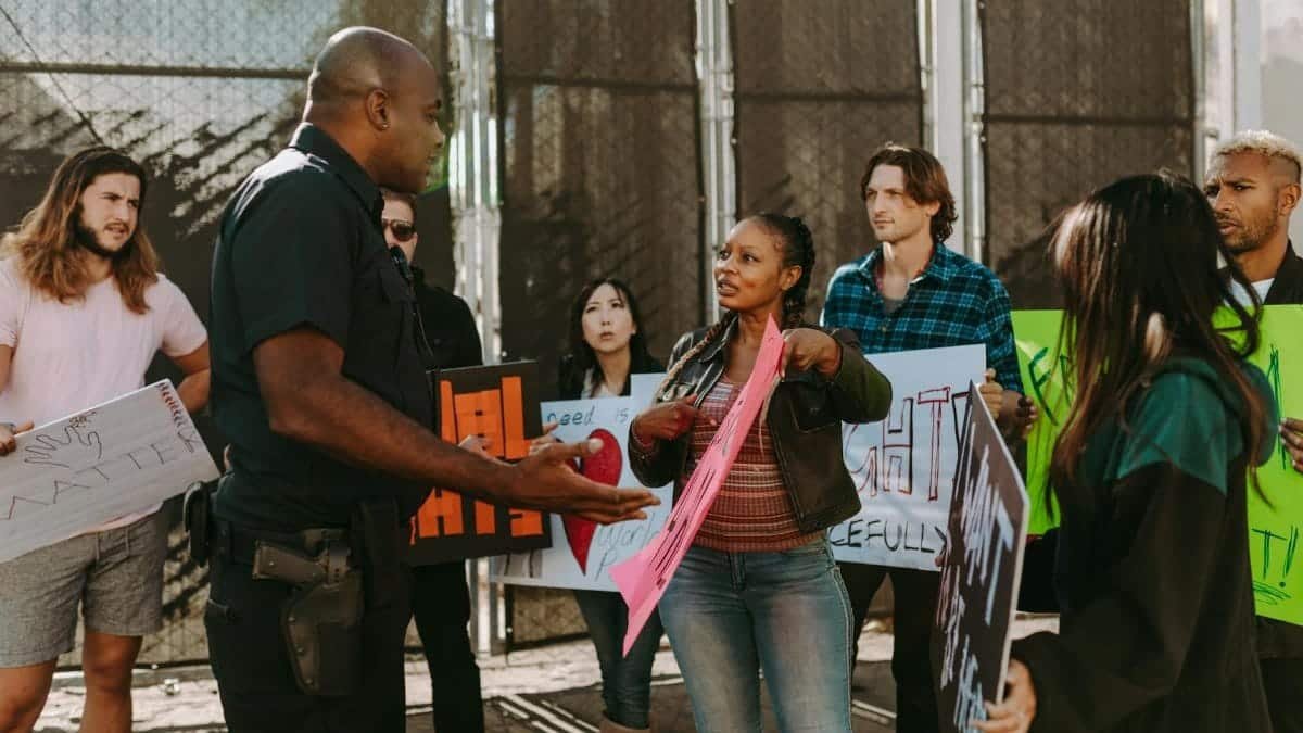 A diverse group of people engaged in a peaceful protest outdoors, discussing with a police officer.