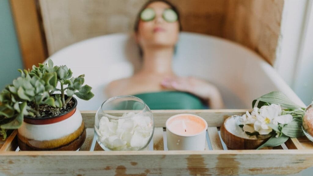 Woman relaxing in a bathtub with a candle and plants, enjoying a serene spa experience.