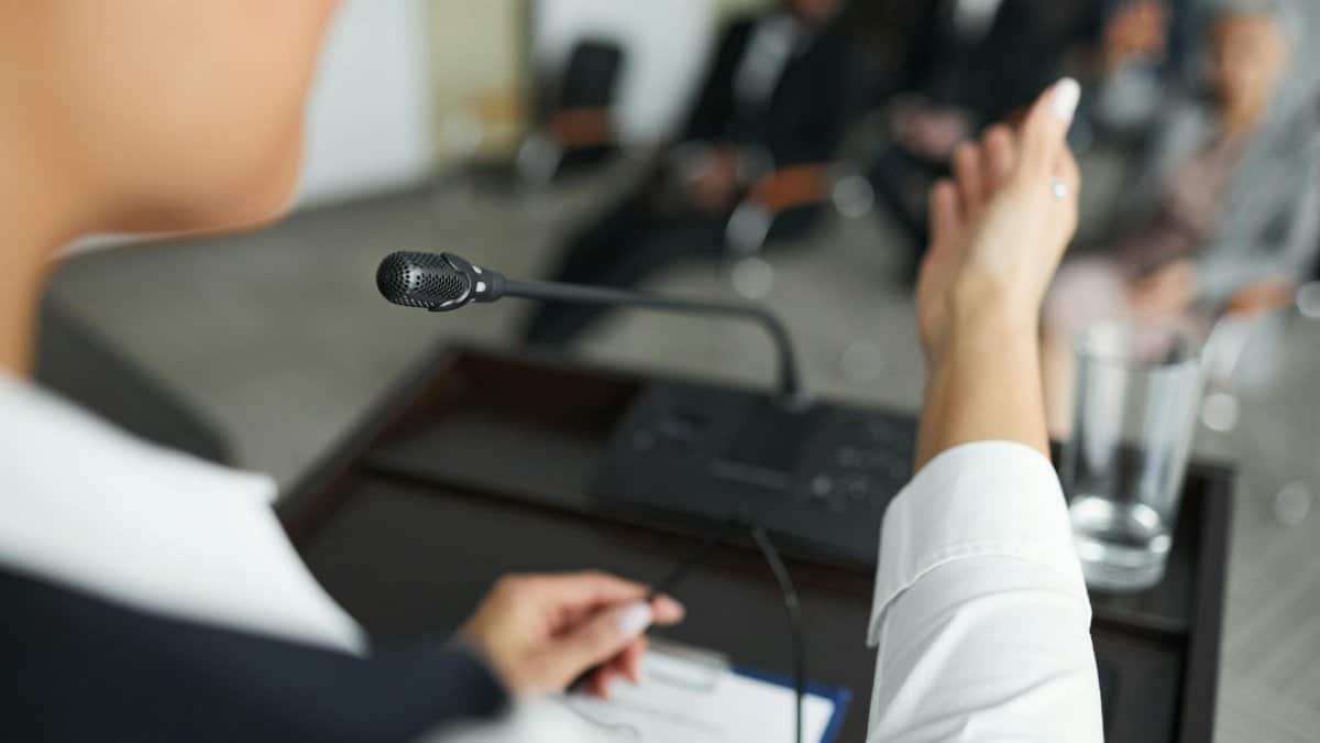 A person speaking at a podium with a microphone to an audience during a business meeting.
