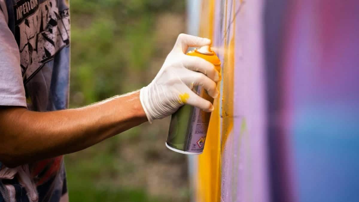 Close-up of a person spray painting a wall outdoors using a glove.