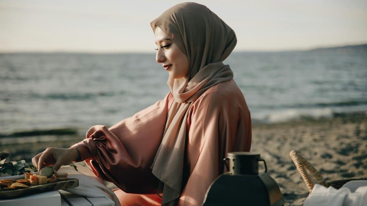 Woman in hijab enjoying a peaceful beach picnic during summer.