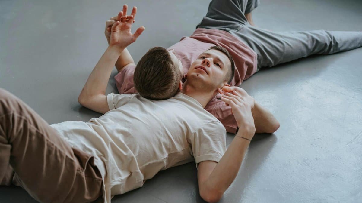 Two men in a loving embrace lie on the floor, exuding a peaceful and intimate moment.