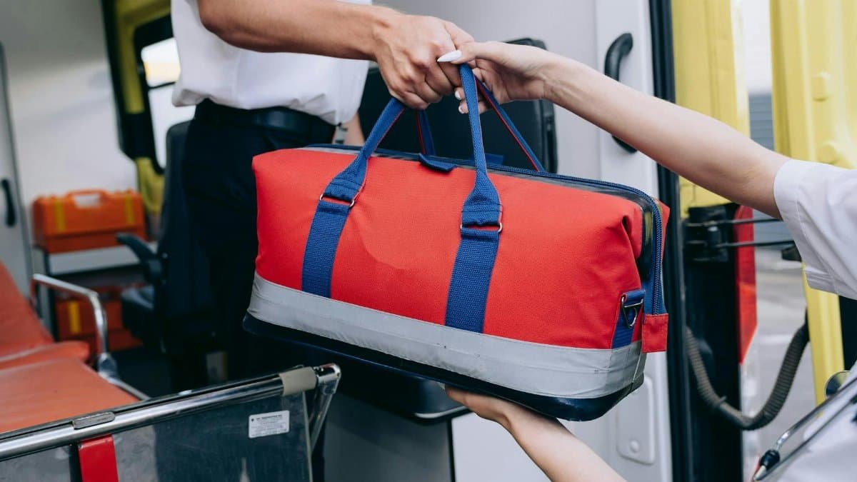 Paramedics exchanging a red medical bag inside an ambulance, demonstrating teamwork.