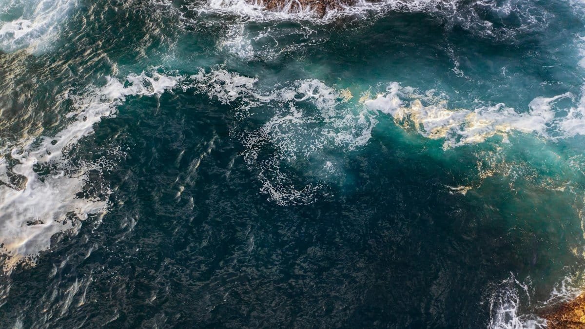 Dramatic aerial shot of ocean waves crashing against rocky shoreline, capturing the vibrant blue and white waters.