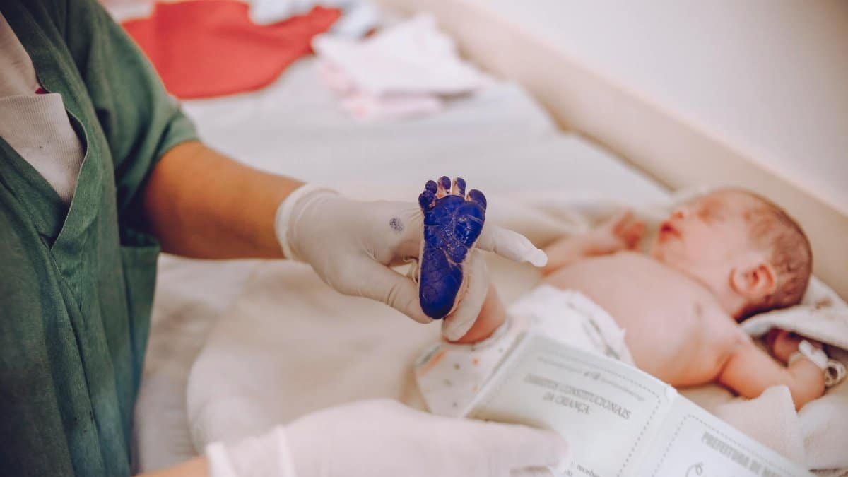 Medical professional taking footprint of a newborn baby in hospital setting.