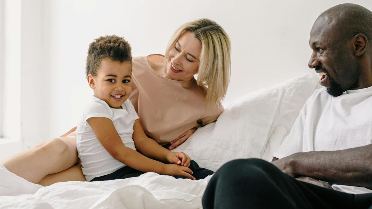 A joyful family spending quality time together on a cozy white bed, sharing smiles and laughter.