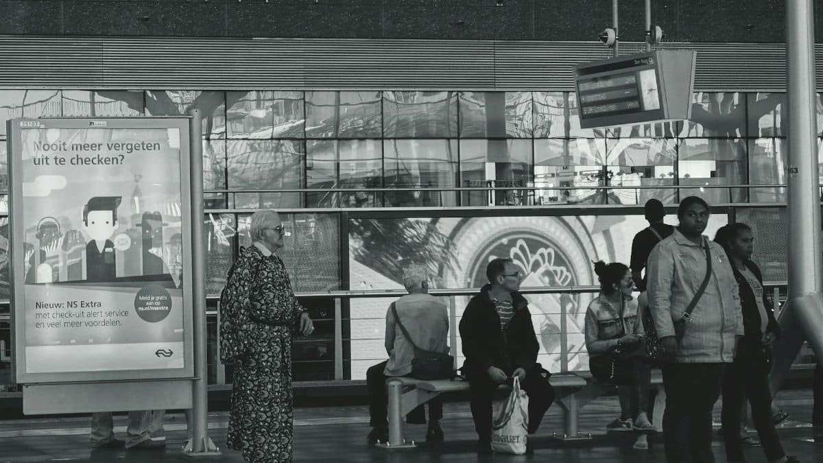 Black and white image of people waiting at a railway station, capturing daily travel life.