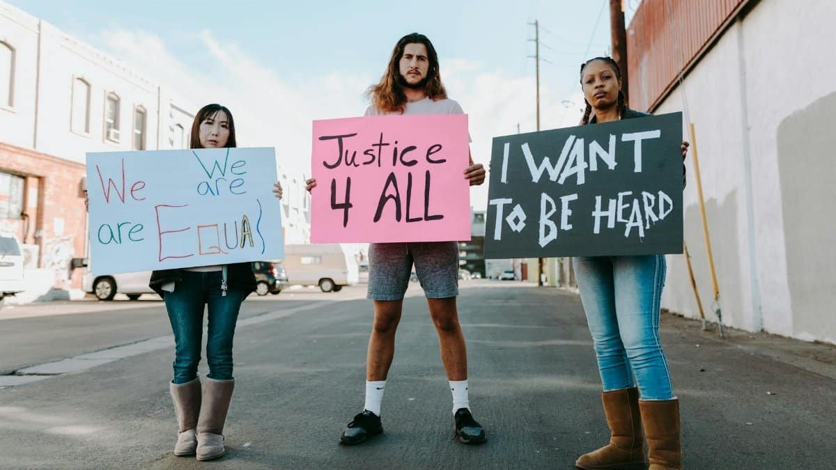 A diverse group of protesters holding signs for equality and justice during a daytime rally.