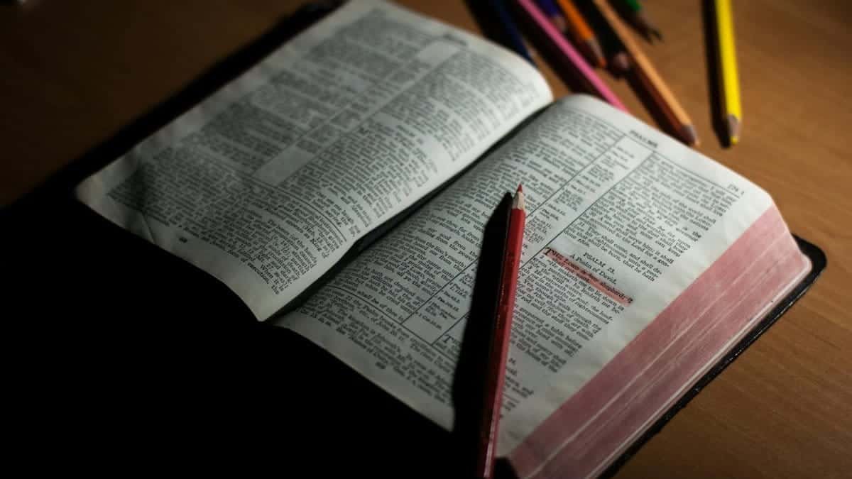 An open Bible on a wooden table accompanied by colored pencils, symbolizing study and spirituality.