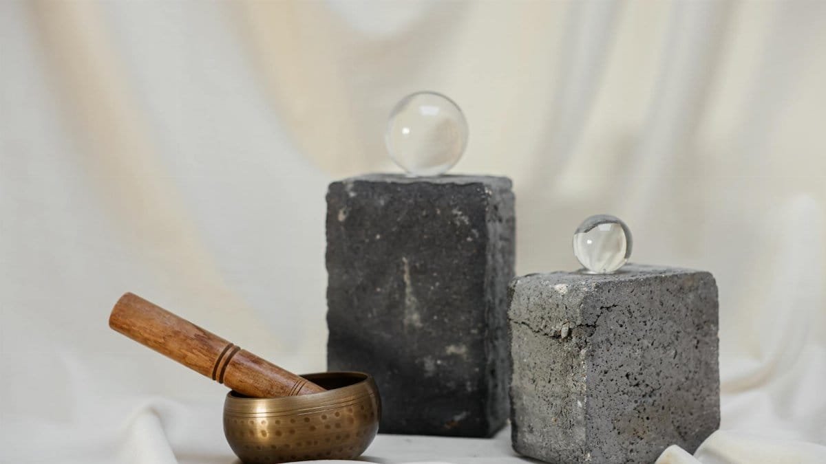 A minimalist composition featuring a crystal ball, singing bowl, and concrete blocks on a soft background.
