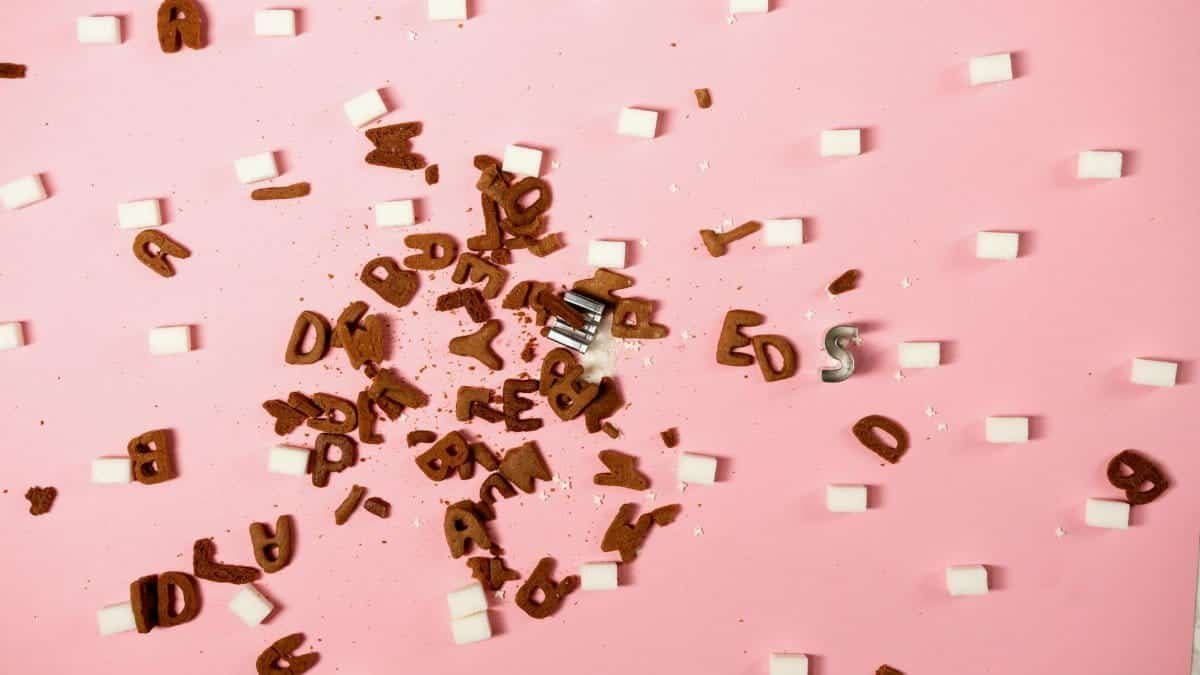 Scattered letters and sugar cubes on a pink background creating an artistic concept.