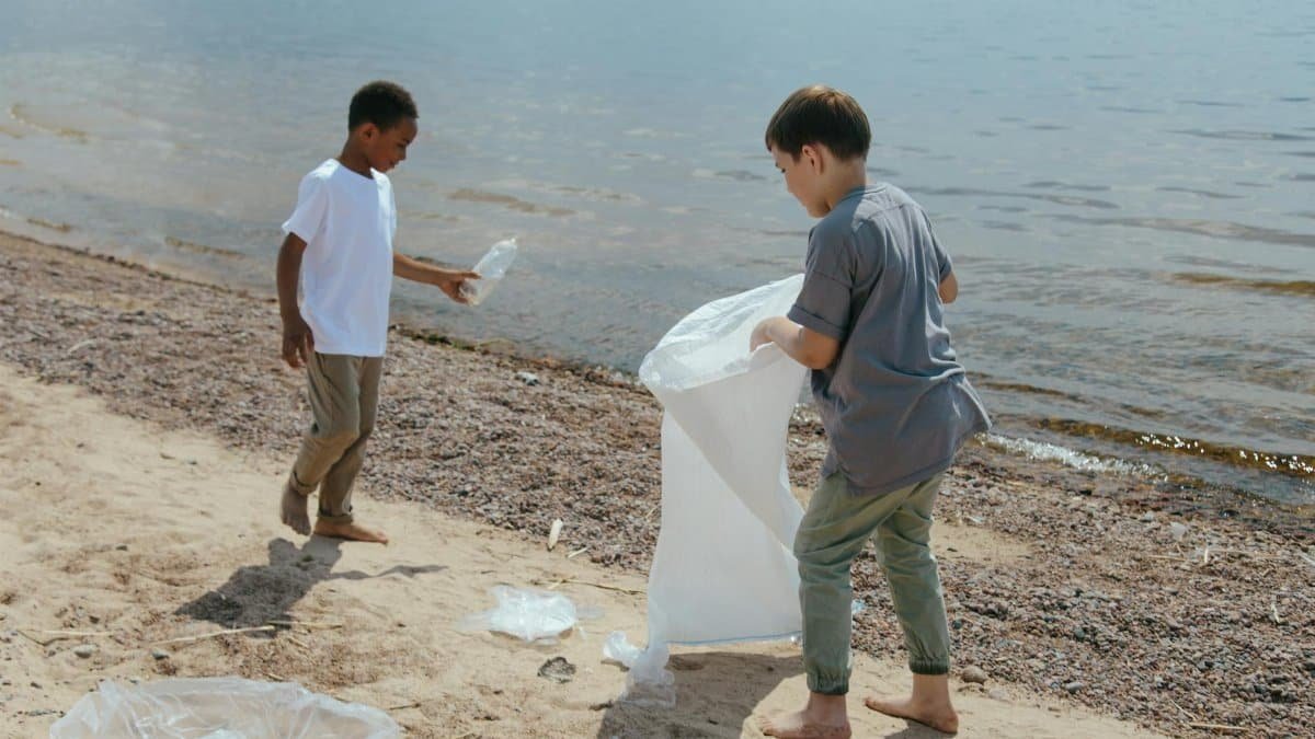 Two boys collect garbage at the beach, promoting volunteerism and environmental care.