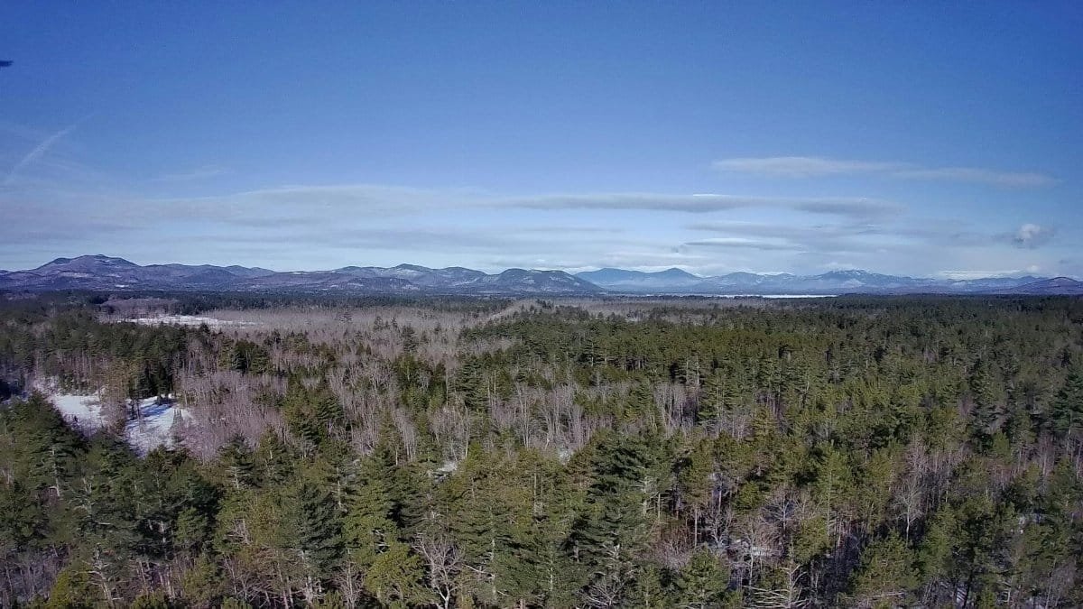 Breathtaking aerial view of a snowy forest and mountains in New Hampshire during winter.