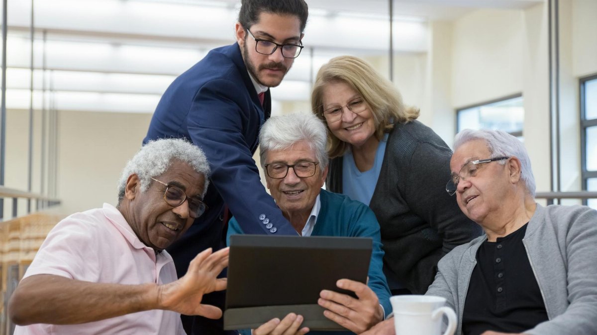 Group of seniors and a young man collaborating using a tablet during a meeting indoors.