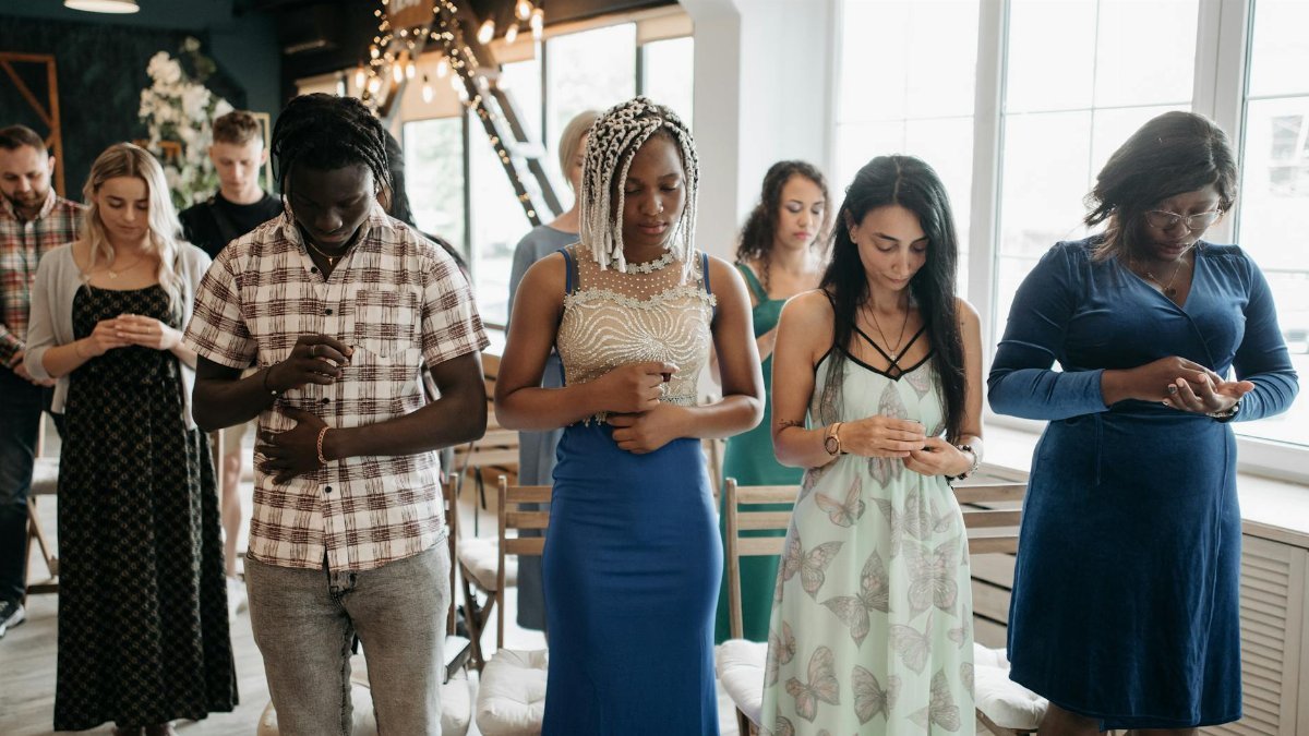 Diverse group of adults praying with heads bowed during an indoor religious gathering.