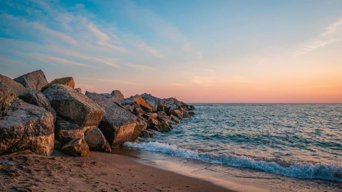 A serene sunset view over the rocky beach in Toronto, Canada. Waves gently crash against the shore.