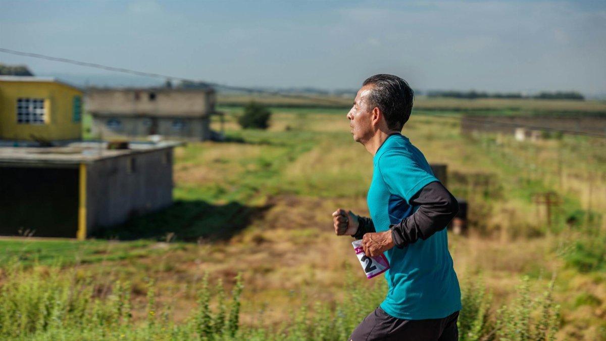 A man jogs in rural area wearing sportswear, emphasizing fitness and determination.