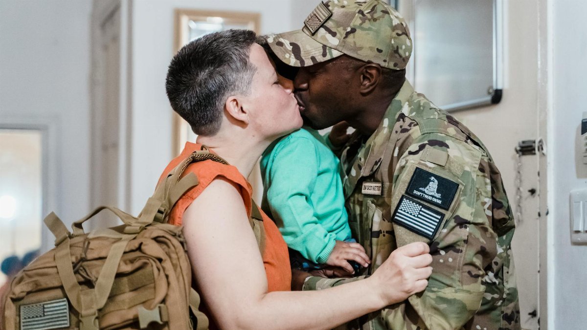 A touching homecoming moment of a soldier in uniform kissing their partner indoors.