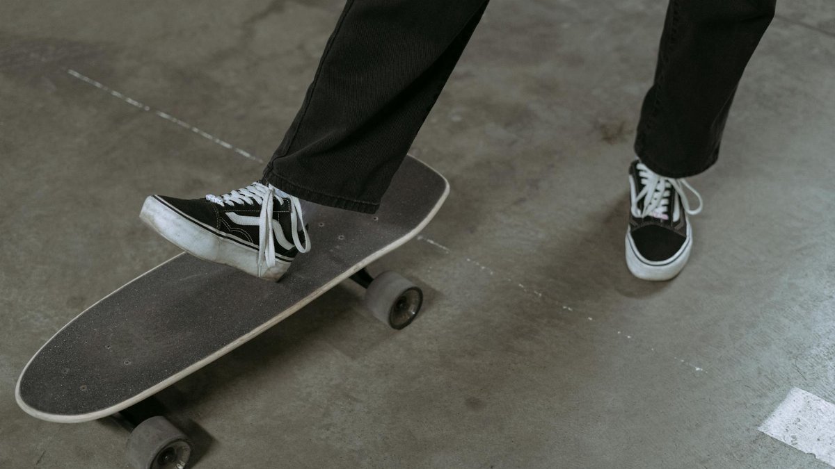 A person wearing sneakers balances on a skateboard indoors, ready to ride.