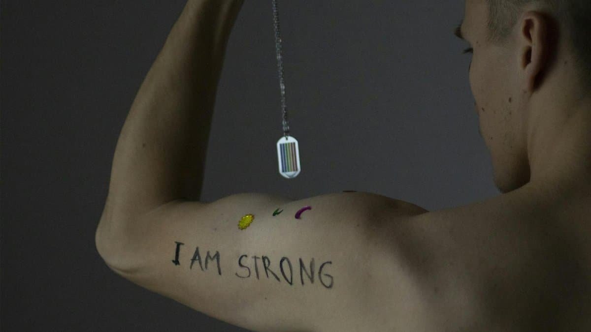 Studio portrait of a shirtless man showcasing 'I Am Strong' tattoo on arm.
