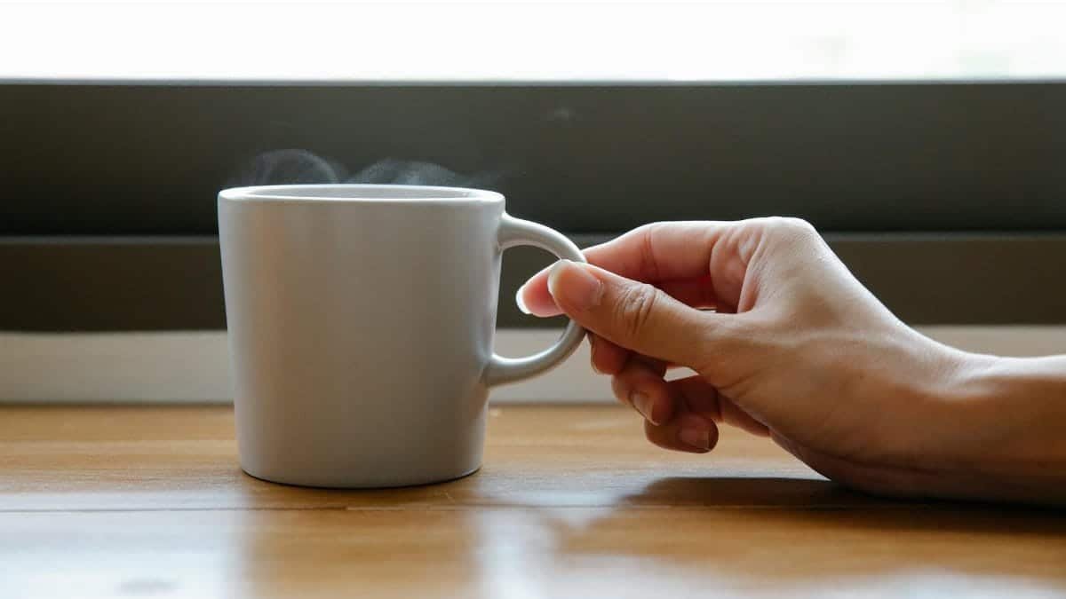 A serene morning scene featuring a hand reaching for a steaming mug of coffee on a wooden table.