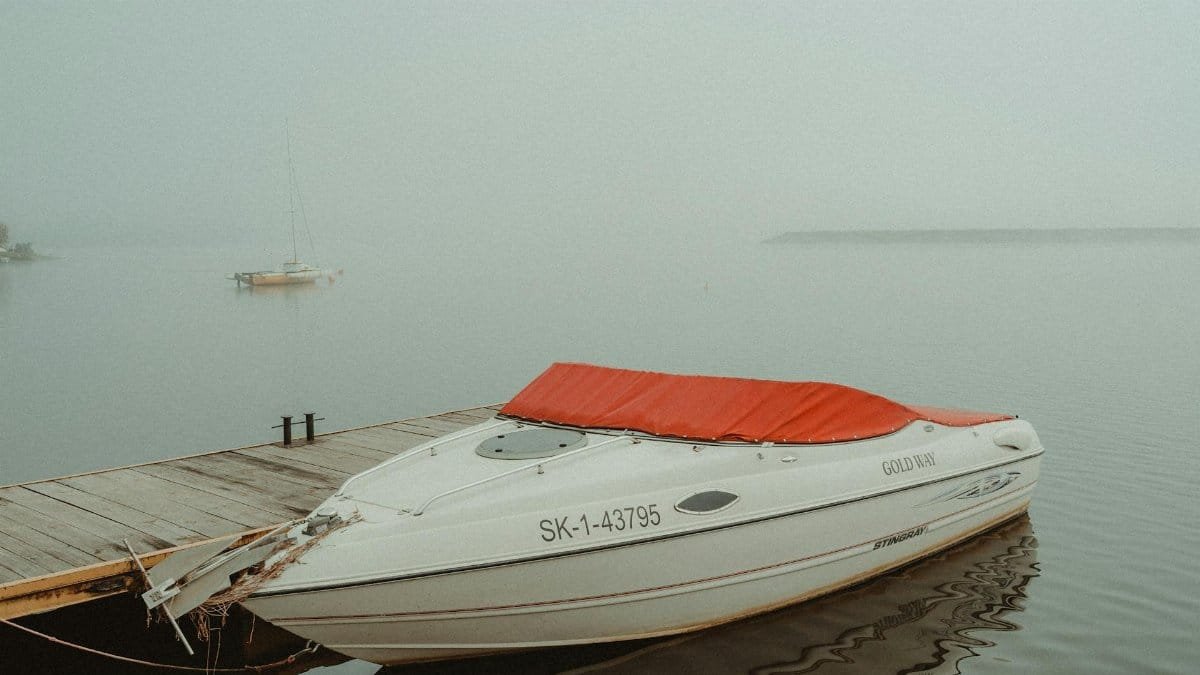 A serene foggy morning at a dock with a moored stingray boat and calm waters.