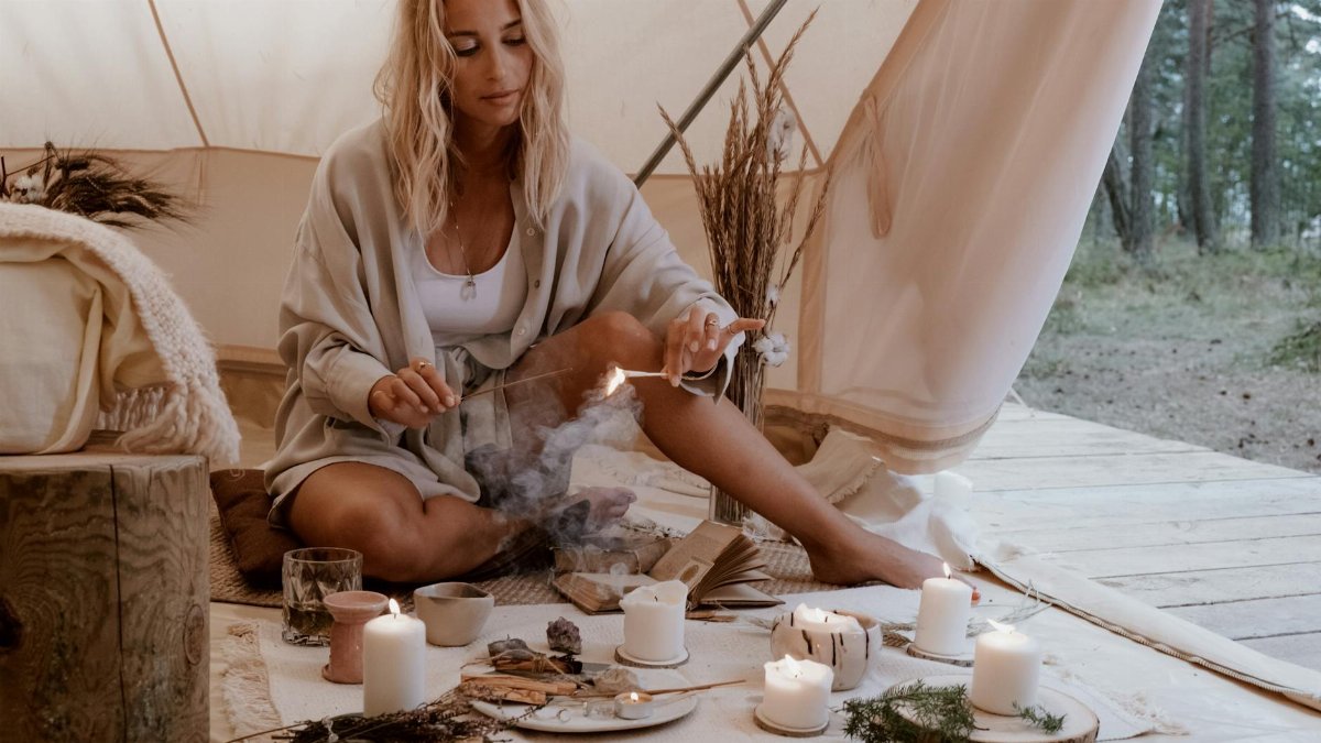 A woman enjoys a tranquil morning in a glamping tent, surrounded by candles and tea, embracing nature's serenity.