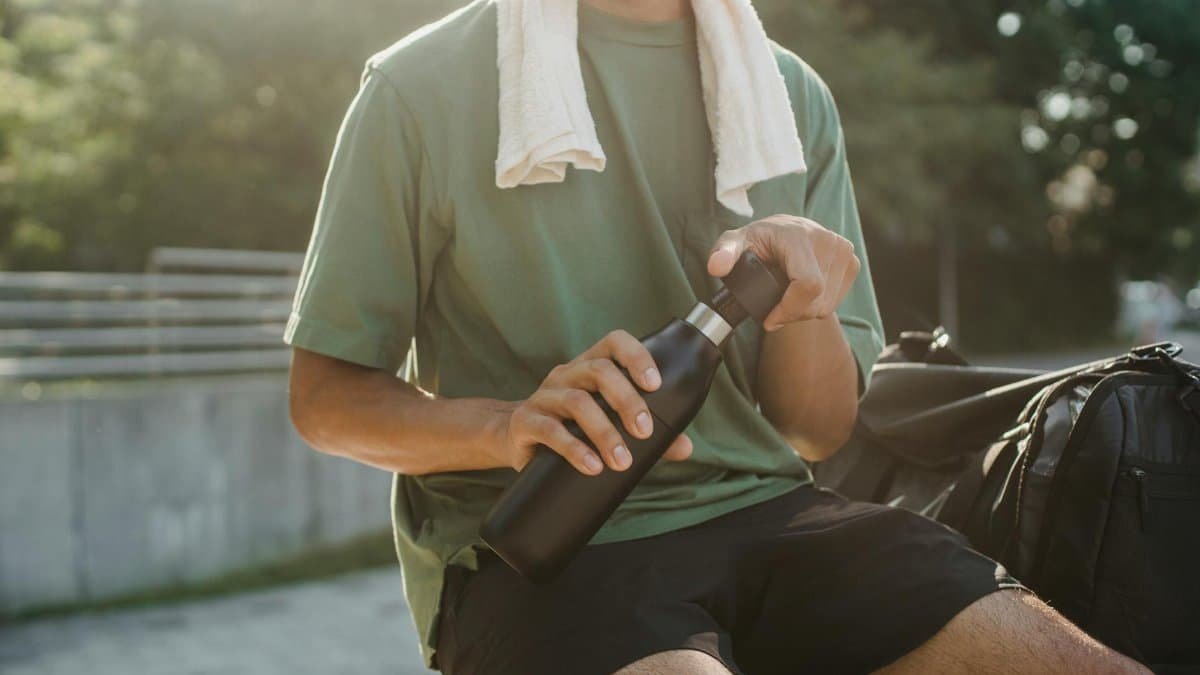 Close-up of a man sitting outdoors with a reusable water bottle and towel.